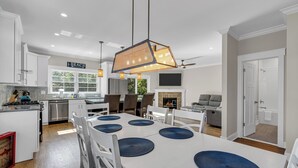 A modern kitchen with white cabinets, a dining area with a white table and blue placemats, and a sign that reads "BEACH". - Prof Cleaned | Pup Friendly | Linen+Towel | Coffee (Seaside Park)