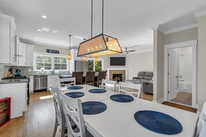 Une cuisine moderne avec des meubles blancs, un coin repas avec une table blanche et des sets de table bleus, et un panneau sur lequel on peut lire « PLAGE ».