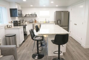 A modern kitchen with white cabinets, a stainless steel refrigerator, a microwave, and a large island with bar stools. - Provo 3-bedroom; new, fireplace, BBQ, AC, fast WiFi. Close to BYU, MTC, Sundance (Provo)