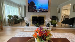 A modern living room with a large flat-screen TV mounted on a brick wall, a fireplace, and a dining area in the background. - Apartment in Perry Hall area (Nottingham)
