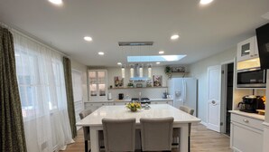 A modern kitchen with a central island, white cabinetry, and a dining area with chairs. - Apartment in Perry Hall area (Nottingham)