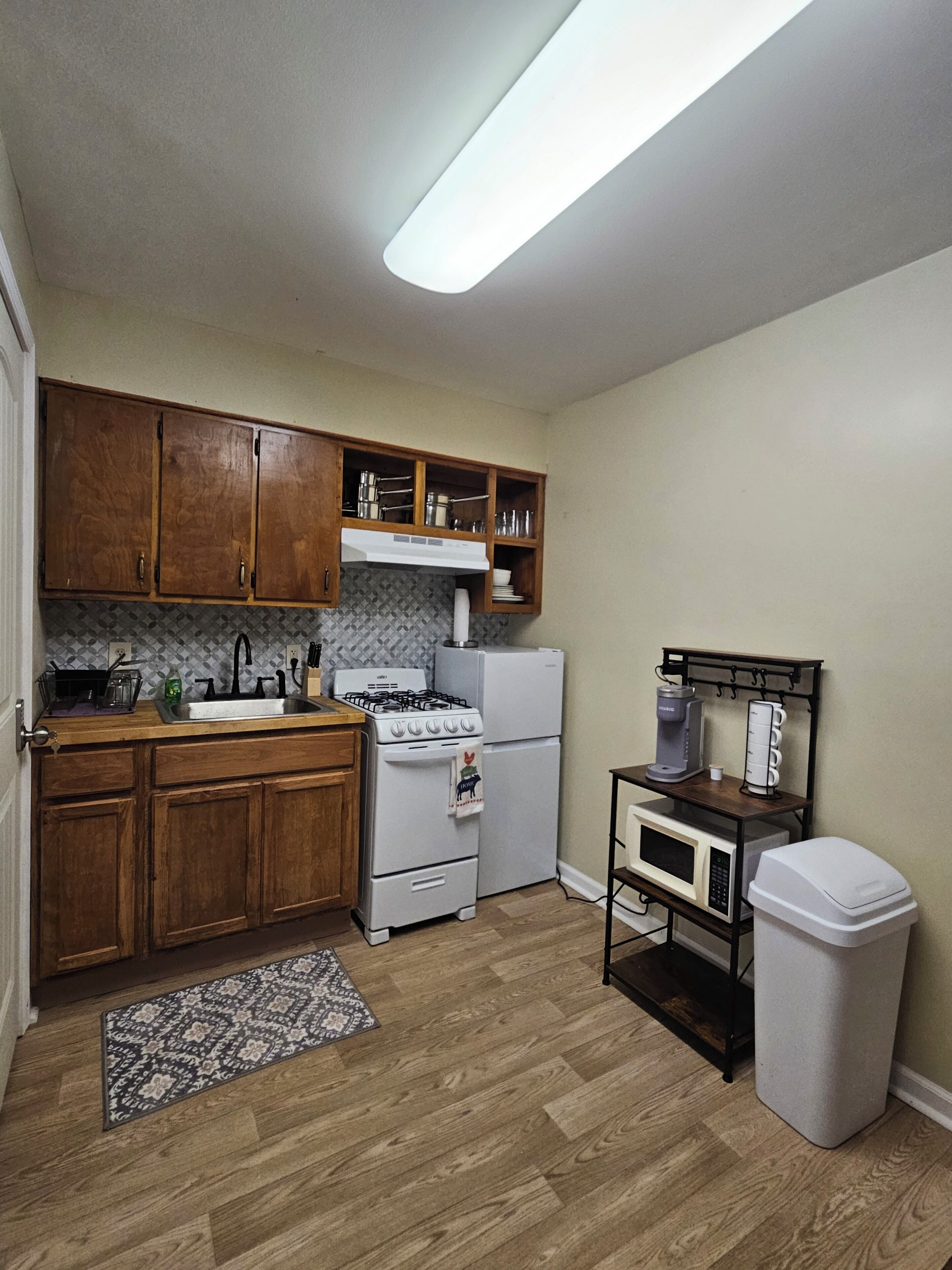 Une cuisine avec des meubles de rangement en bois, une cuisinière, un réfrigérateur, un four à micro-ondes et une poubelle.