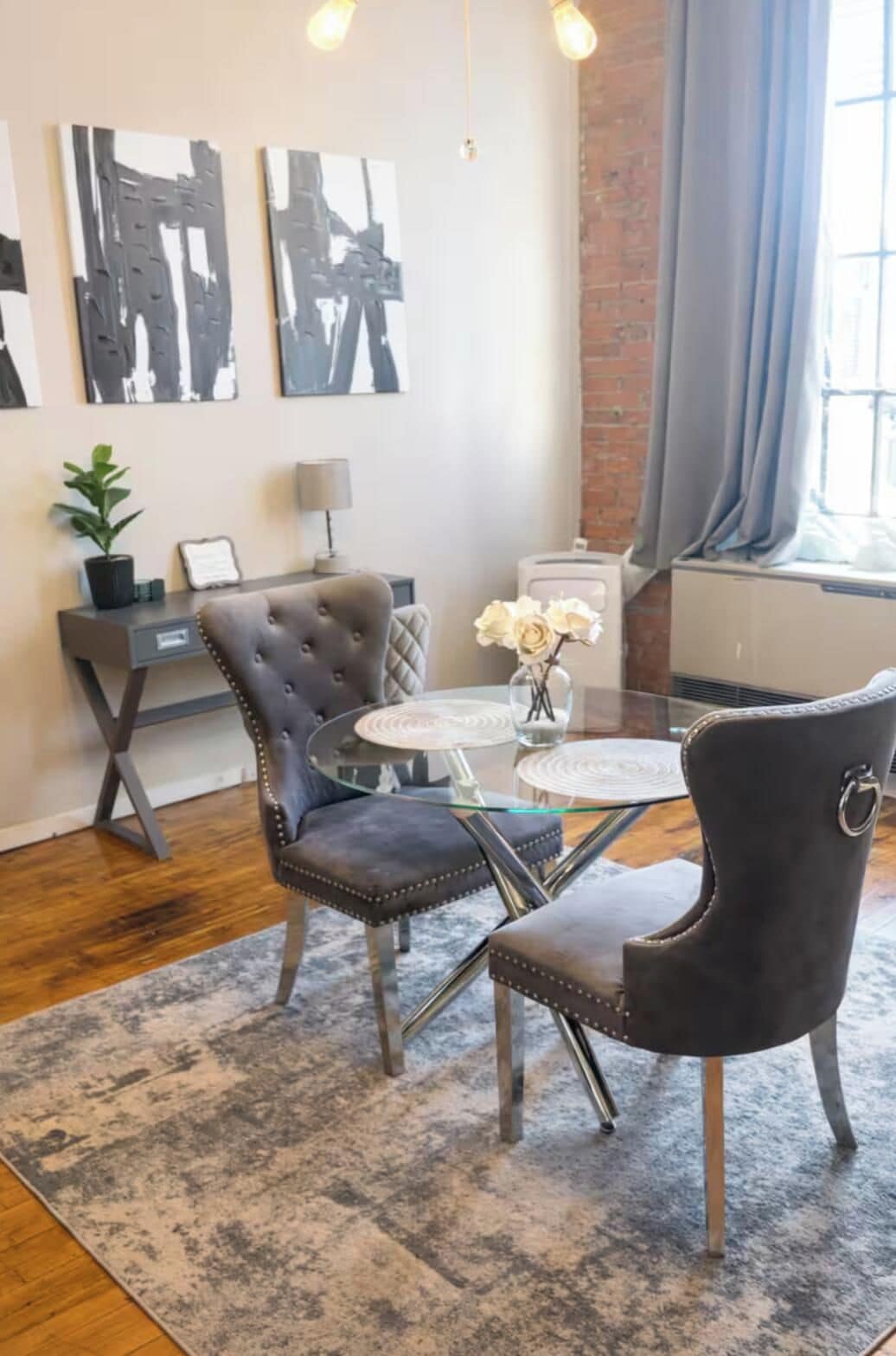 A modern living room with a glass coffee table, two upholstered chairs, a potted plant, and abstract wall art.