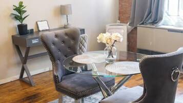 A modern living room with a glass coffee table, two upholstered chairs, a potted plant, and abstract wall art.
