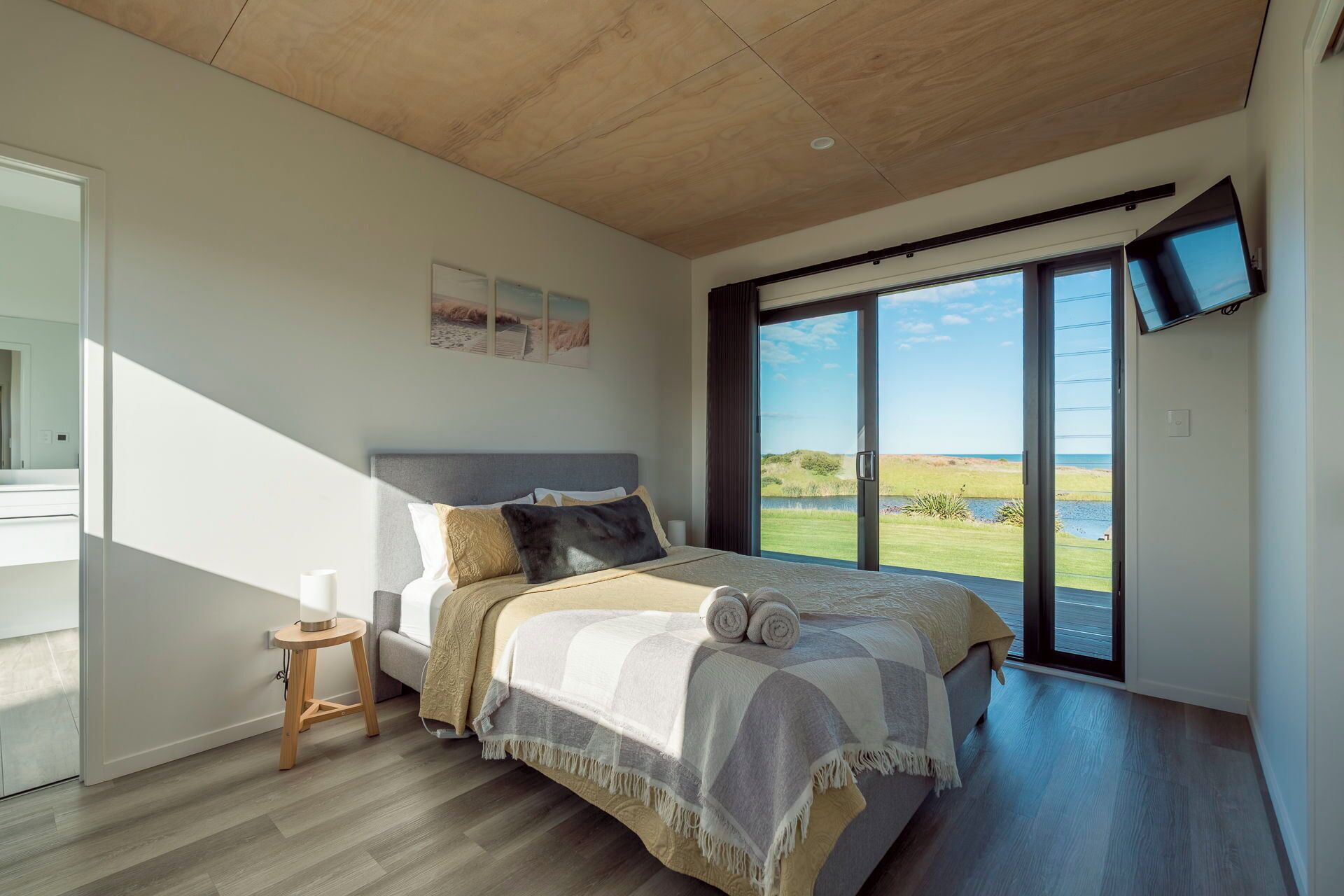 Ein Schlafzimmer mit einem großen Bett, einem kleinen Nachttisch, einem an der Wand befestigten Fernseher und einer Schiebetür zu einem Ausblick ins Freie.