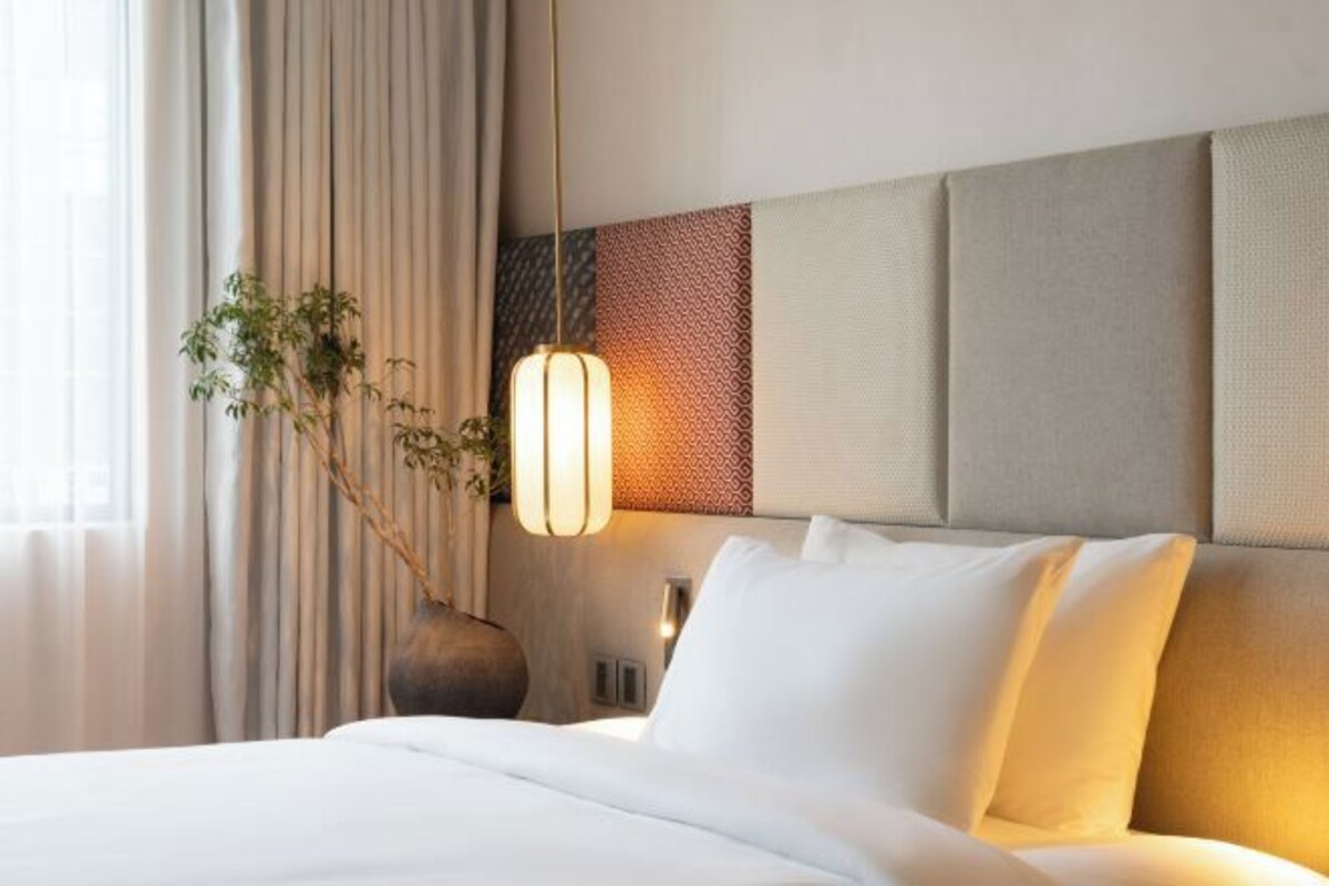 Une chambre d’hôtel avec un lit, une lampe suspendue, une plante et un panneau mural texturé.