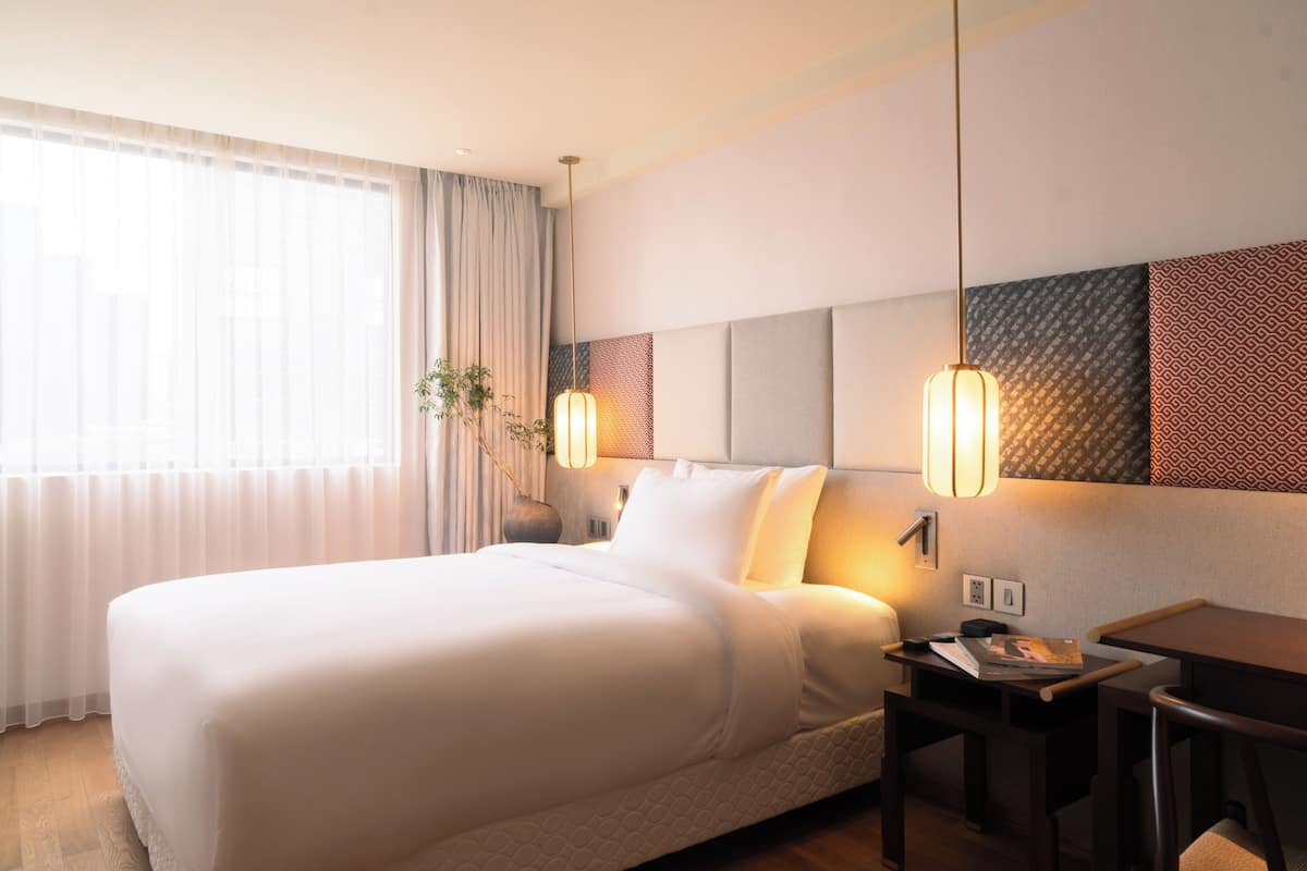 Ein Hotelzimmer mit einem großen Bett, Nachttischen, einem Schreibtisch und einem Fenster mit Vorhängen.