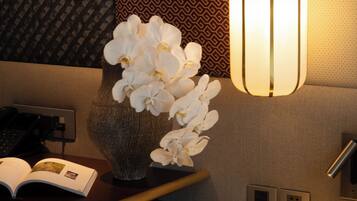 Een hotelkamer met nachtkastje, een vaas witte orchideeën, een boek, een afstandsbediening en een lamp.