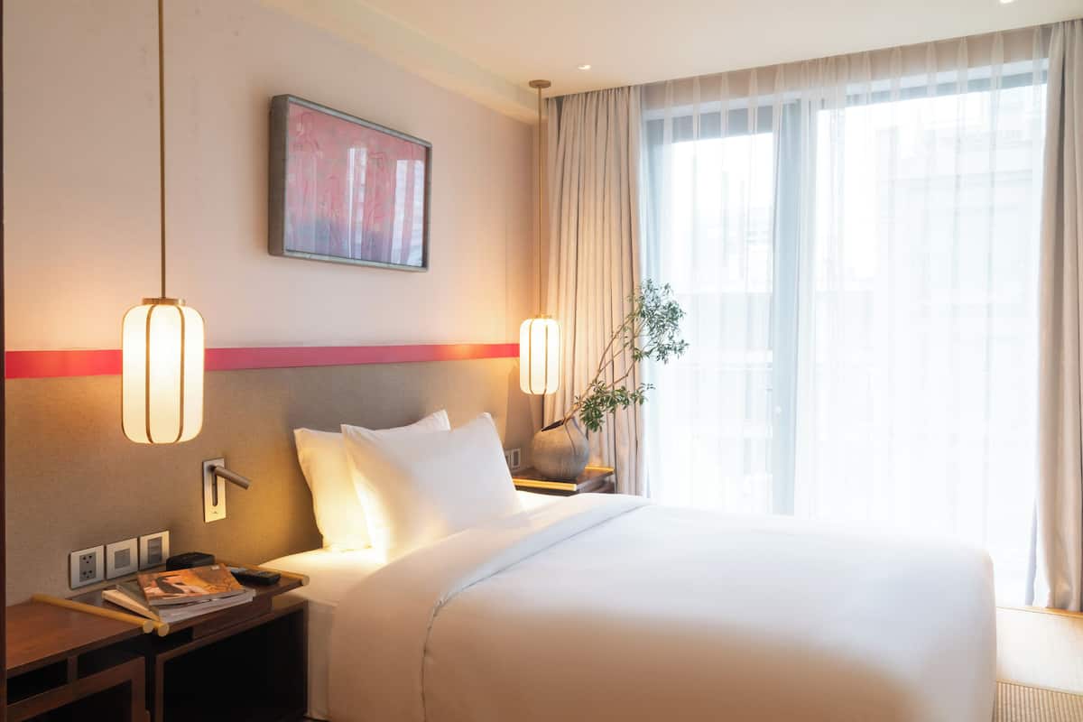 Ein Hotelzimmer mit einem großen Bett, Nachttischen, einem Wandbild und einem Fenster mit Vorhängen.