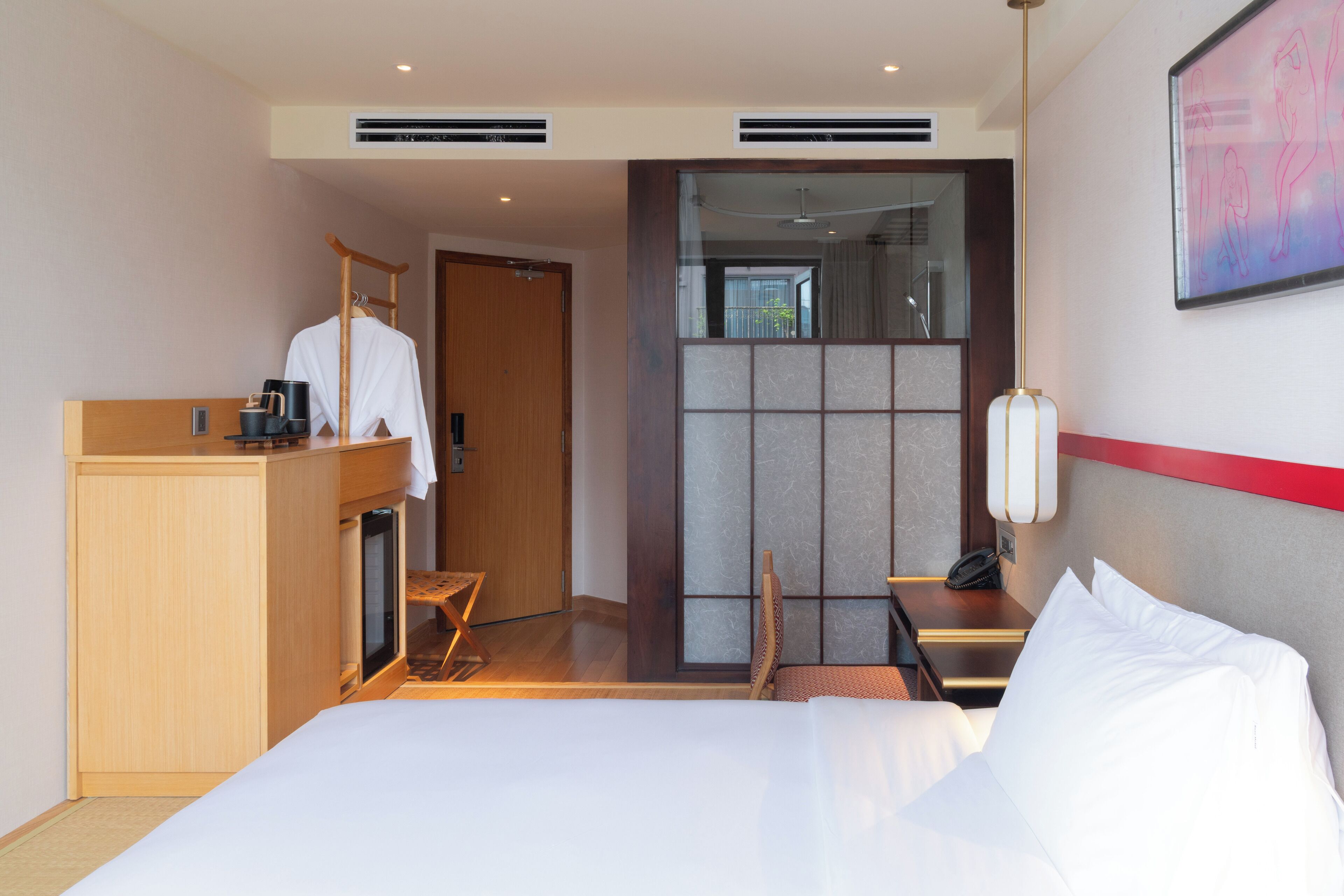 Una habitación de hotel con cama, escritorio y silla, armario, y una puerta corredera que da al baño.