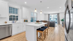 A modern kitchen with white cabinetry, a central island with stools, and a stainless steel refrigerator. - 3 Stories w/86" TV | Keurig | Pro Cleaned | Garage (Seaside Heights)