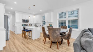 A modern kitchen with white cabinets, a central island, and a dining area with chairs. - 3 Stories w/86" TV | Keurig | Pro Cleaned | Garage (Seaside Heights)