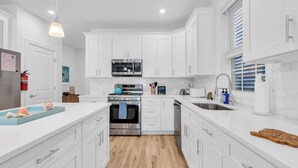 A modern kitchen with white cabinets, stainless steel appliances, and a wooden floor. - 3 Stories w/86" TV | Keurig | Pro Cleaned | Garage (Seaside Heights)
