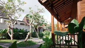 A covered outdoor area with a wooden structure, surrounded by large green plants and trees. - The Riang Villa (Kerobokan)