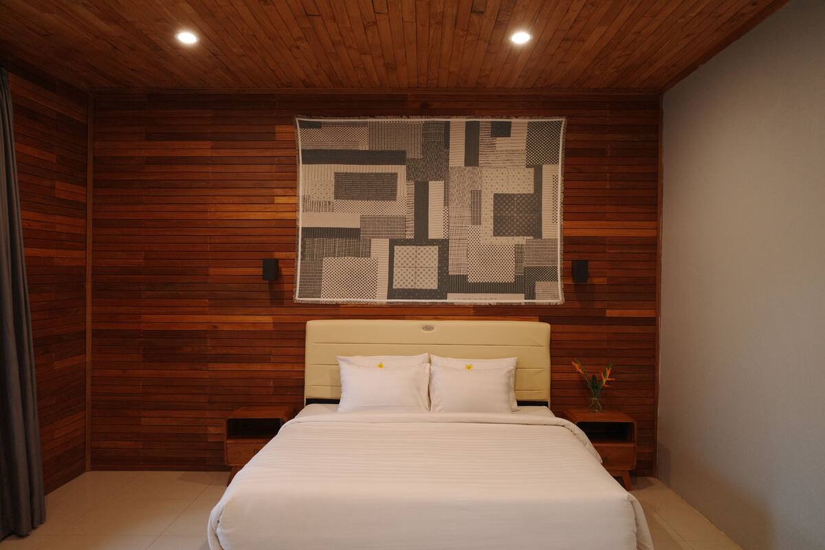 Un dormitorio con techo de madera, una cama grande con ropa de cama blanca, cabecero y una obra de arte abstracta colgada en la pared.