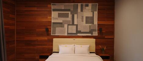 Une chambre avec un plafond en bois, un grand lit avec une literie blanche, une tête de lit et une œuvre d’art abstraite accrochée au mur.