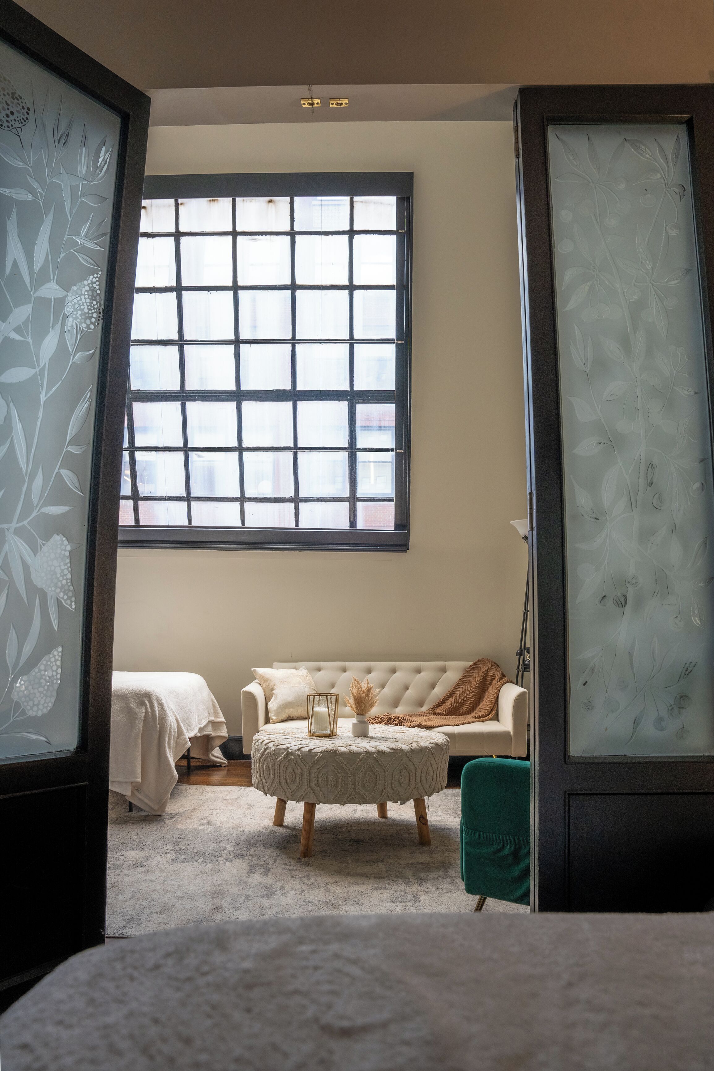 Una habitación con un ventanal grande, un sofá, un reposapiés y una silla verde.