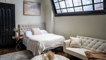 A bedroom with a bed, a white sofa, a window, and a painting on the wall.