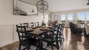 A dining area with a large table, chairs, a chandelier, and a view of the outdoors.