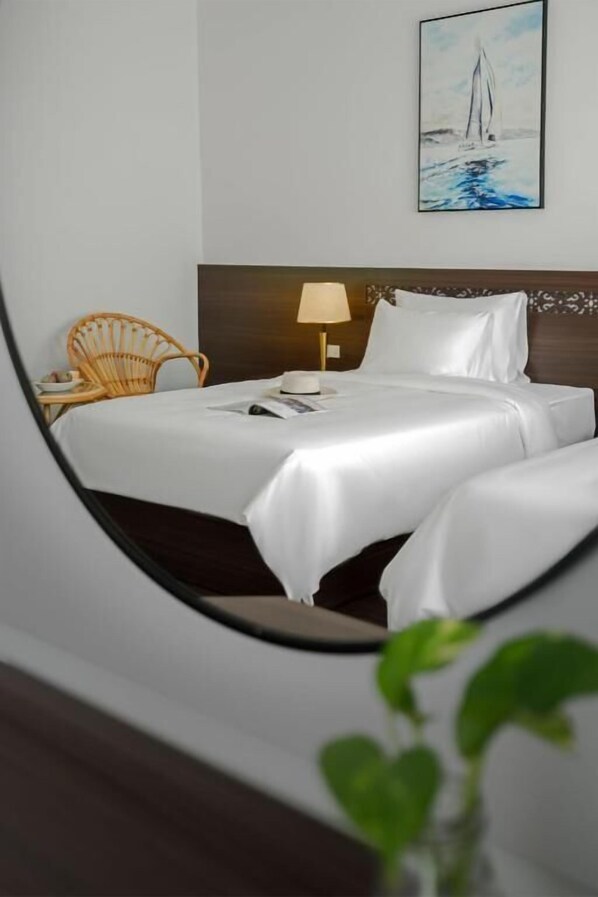 A neatly made bed with white linens, a wooden headboard, a bedside lamp, and a wicker chair. - Hoang Yen Boutique Hotel (Da Nang)