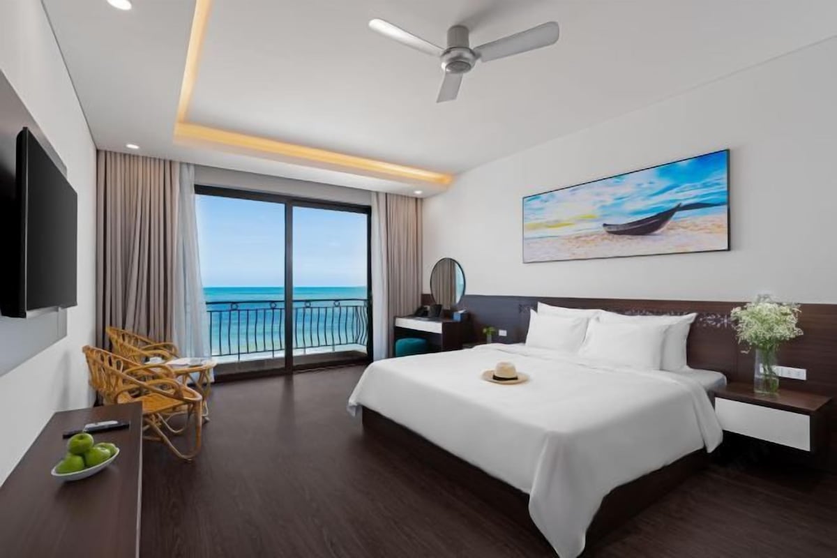 Habitación de hotel con cama, escritorio, silla, televisor, un cuadro y vista al océano.
