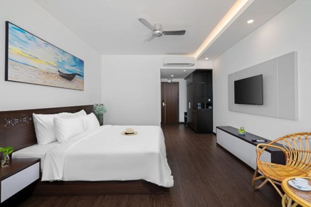 Una habitación de hotel moderna con una cama, un televisor de pantalla plana, un ventilador de techo y un cuadro de un barco en la pared.