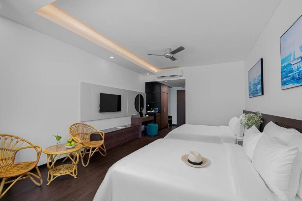 A hotel room with two beds, a desk, a TV, and wicker chairs.