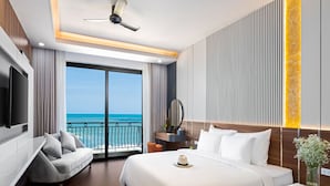 A hotel room with a bed, a TV, a ceiling fan, a desk, and a view of the ocean. - Hoang Yen Boutique Hotel (Da Nang)