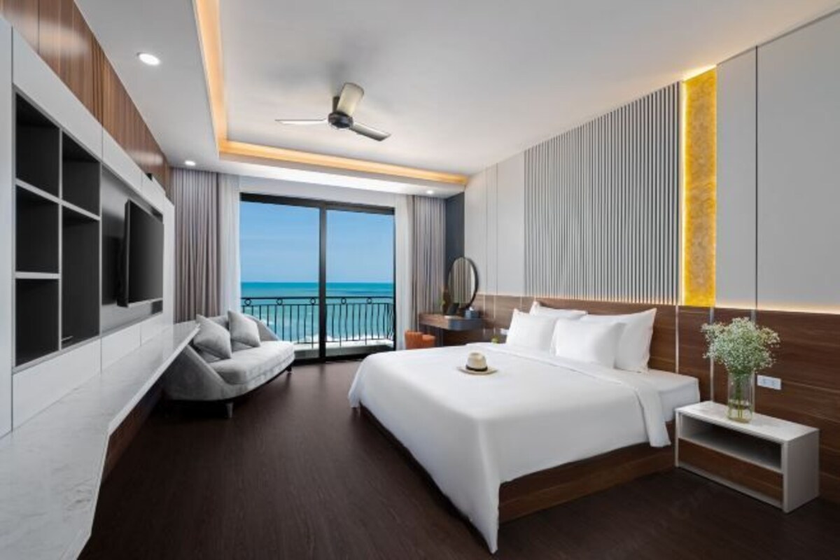 Una habitación de hotel moderna con una cama grande, zona de estar, televisión y vista al océano.