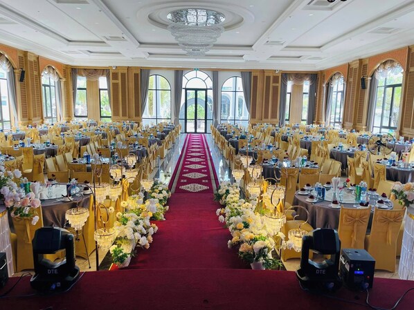 Un salón de banquetes con filas de mesas, sillas doradas y una alfombra roja.