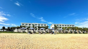 A beachfront hotel with multiple white buildings, palm trees, and umbrellas. - Hoang Yen Boutique Hotel (Da Nang)