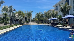 A swimming pool with lounge chairs and umbrellas, surrounded by palm trees and modern buildings. - Hoang Yen Boutique Hotel (Da Nang)