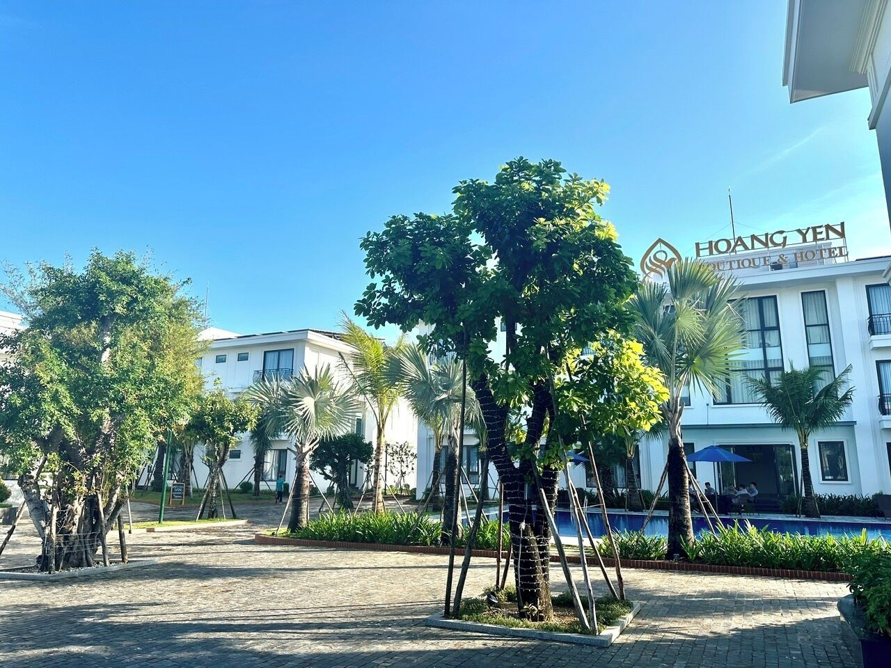Un patio de hotel con árboles, una piscina y un edificio con un cartel que dice "Hoang Yen Boutique & Hotel".