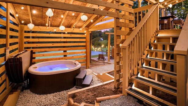 Un espacio tipo spa de madera con un jacuzzi, bancos de madera y una escalera.