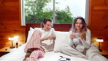 Une chambre avec un plafond en pente, une grande fenêtre, un lit avec des oreillers, et deux personnes qui lisent des livres.
