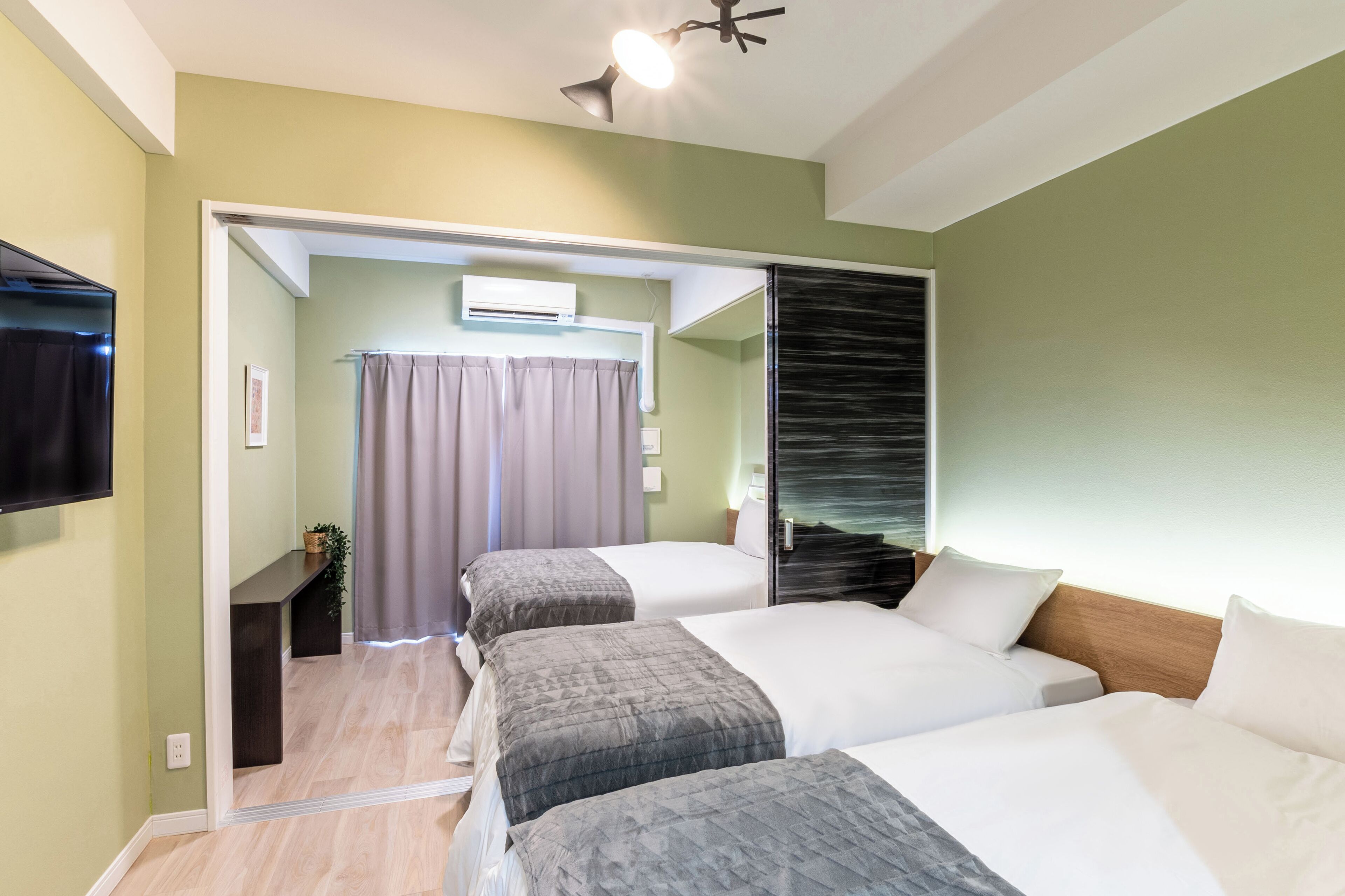 A hotel room with two beds, a television, a window with curtains, and an air conditioning unit.
