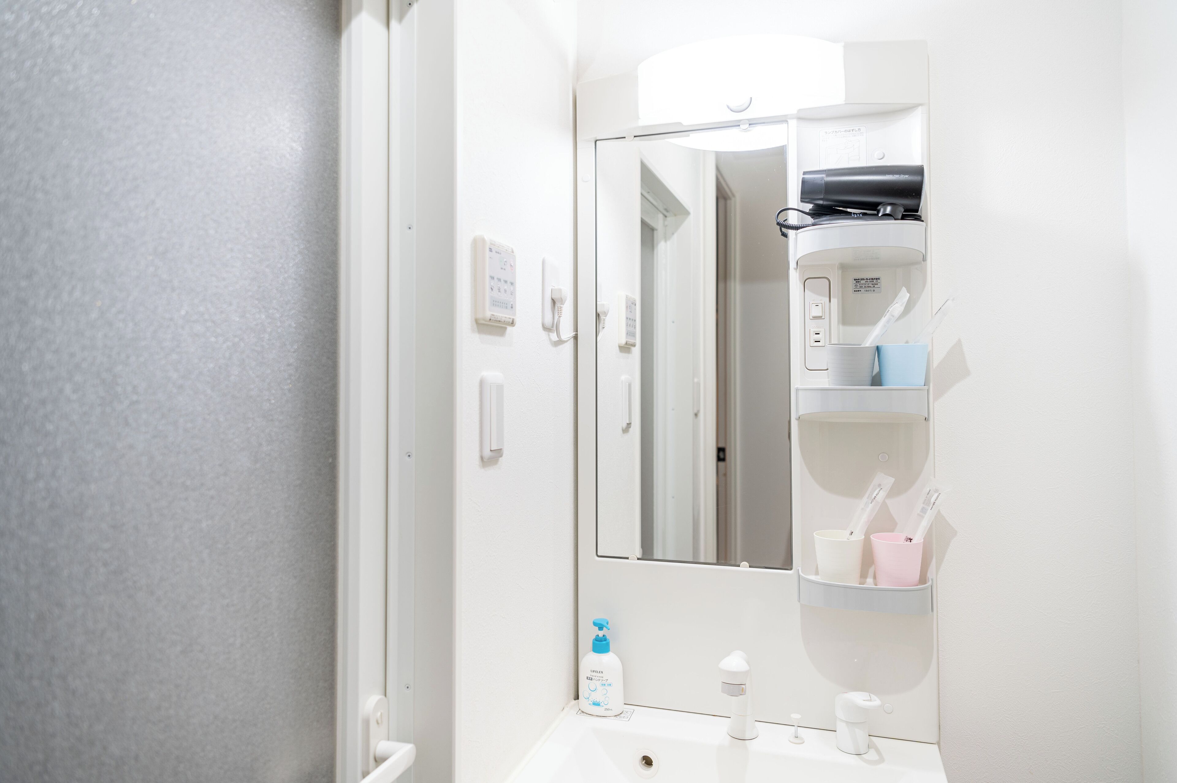 A bathroom with a white sink, a mirror, a hairdryer, and a phone on the wall.