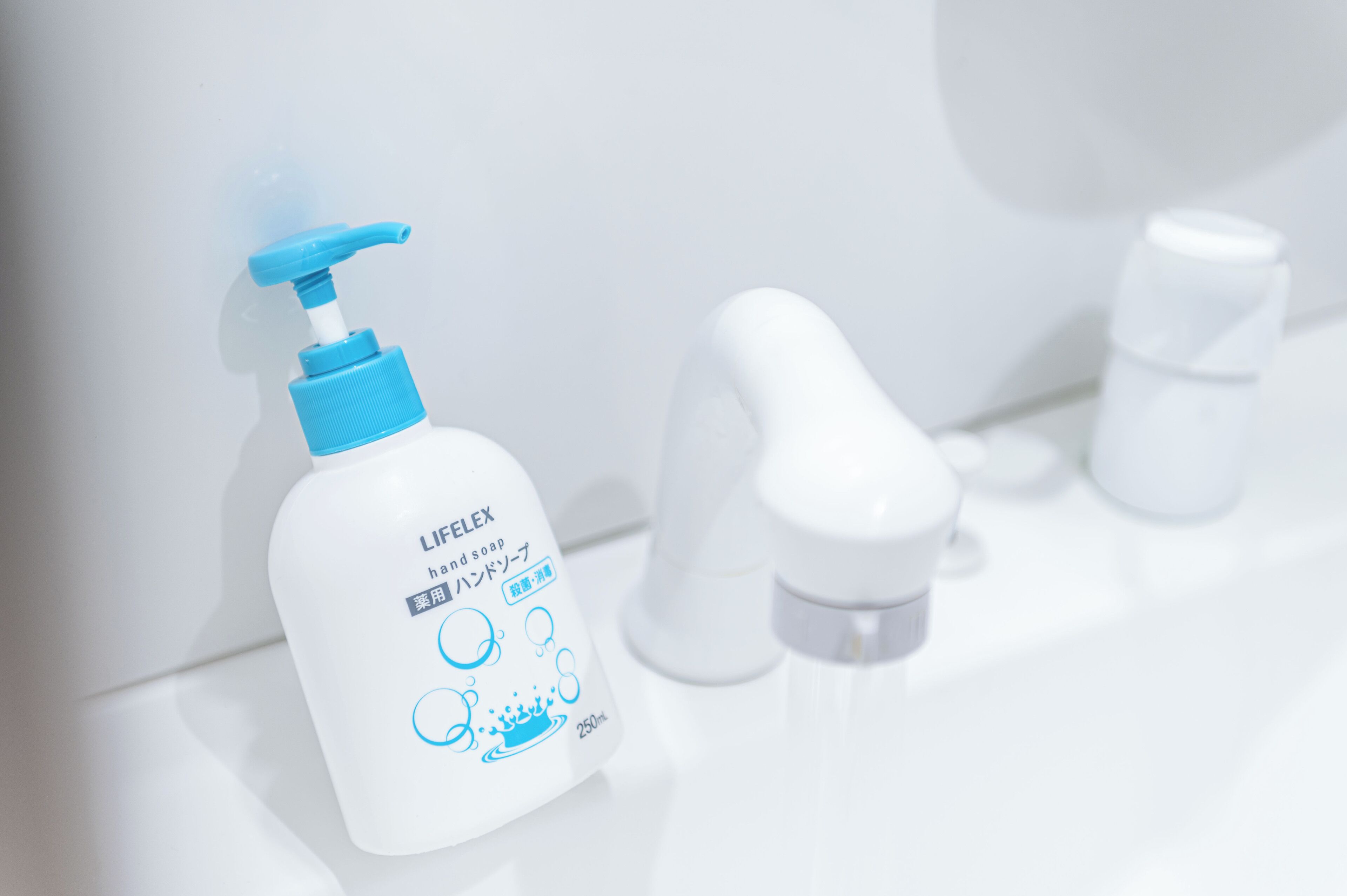 Une salle de bain avec un lavabo blanc, un distributeur de savon liquide et un robinet.