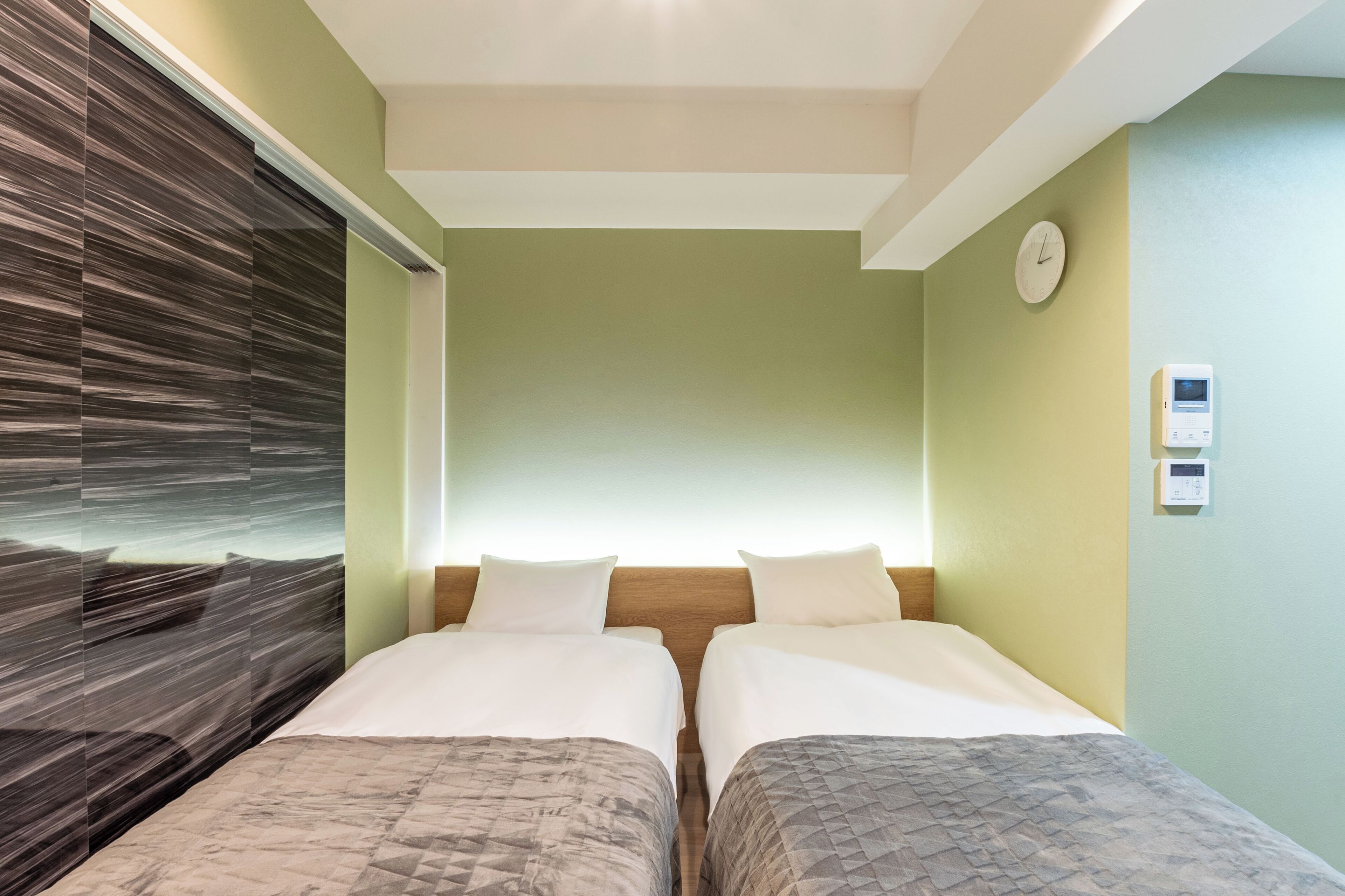 A hotel room with two beds, a wooden headboard, a clock, and a thermostat on the wall.
