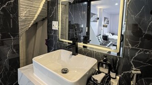 Een moderne badkamer met een grote spiegel, een witte wastafel en zwarte marmeren wanden.