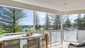 A spacious balcony with a view of a lake and trees, a dining table with chairs, and a striped chair.