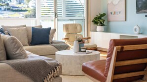 A modern living room with a sofa, a round coffee table, a leather armchair, and a view of the outdoors through large windows.