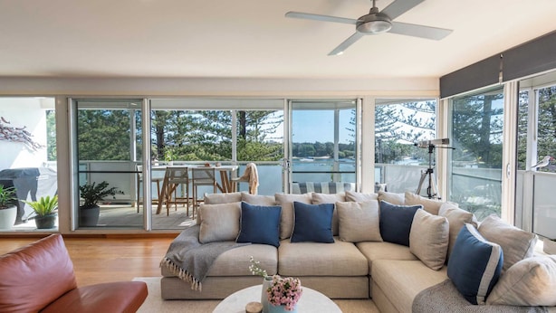 A modern living room with a beige sectional sofa, a round coffee table, and a view of a balcony with outdoor furniture.