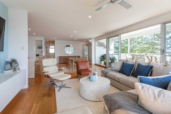 A spacious living room with a large sofa, a coffee table, and a dining area in the background. - Penthouse on the Ritz - Oceanstays (Yamba)