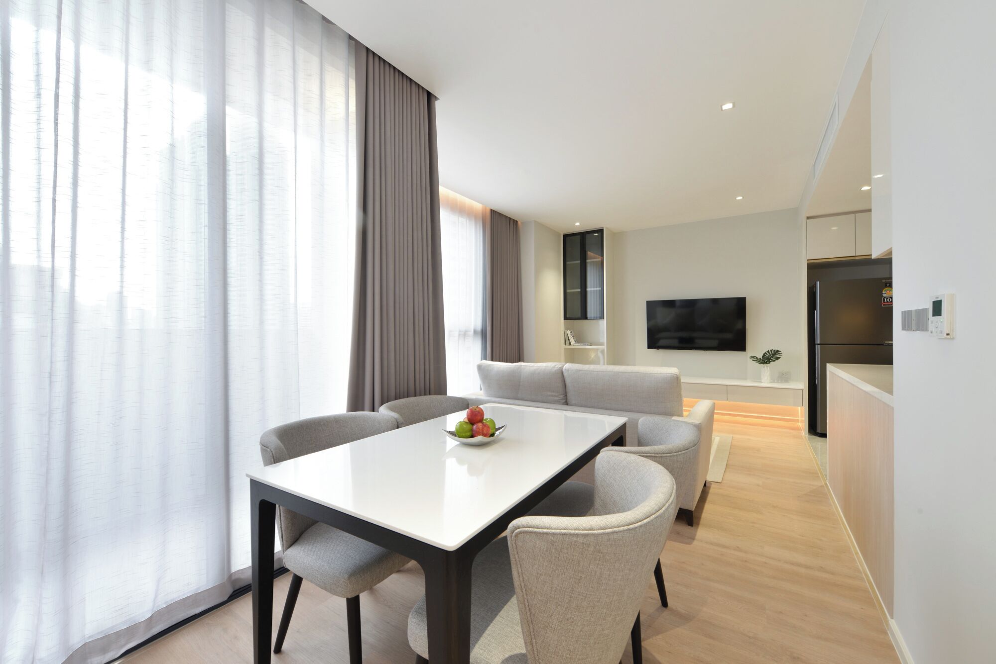 Una sala de estar moderna con una mesa de comedor y sillas, un sofá, un televisor de pantalla plana y una zona de cocina con un refrigerador.
