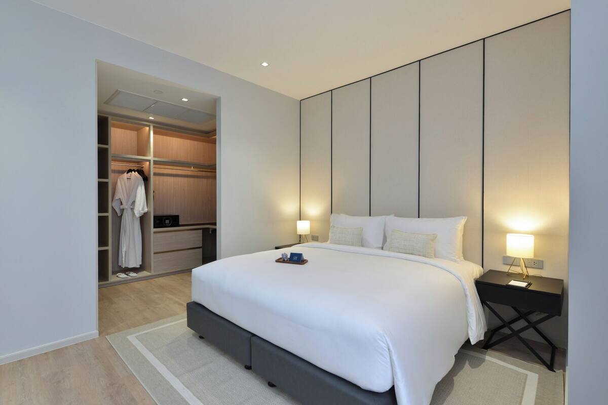 Une chambre d’hôtel moderne avec un grand lit, un dressing et une table de chevet avec une lampe.