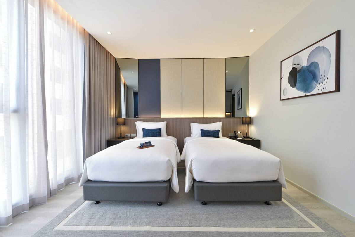 Une chambre d’hôtel moderne avec deux lits, un grand miroir et un tableau au mur.