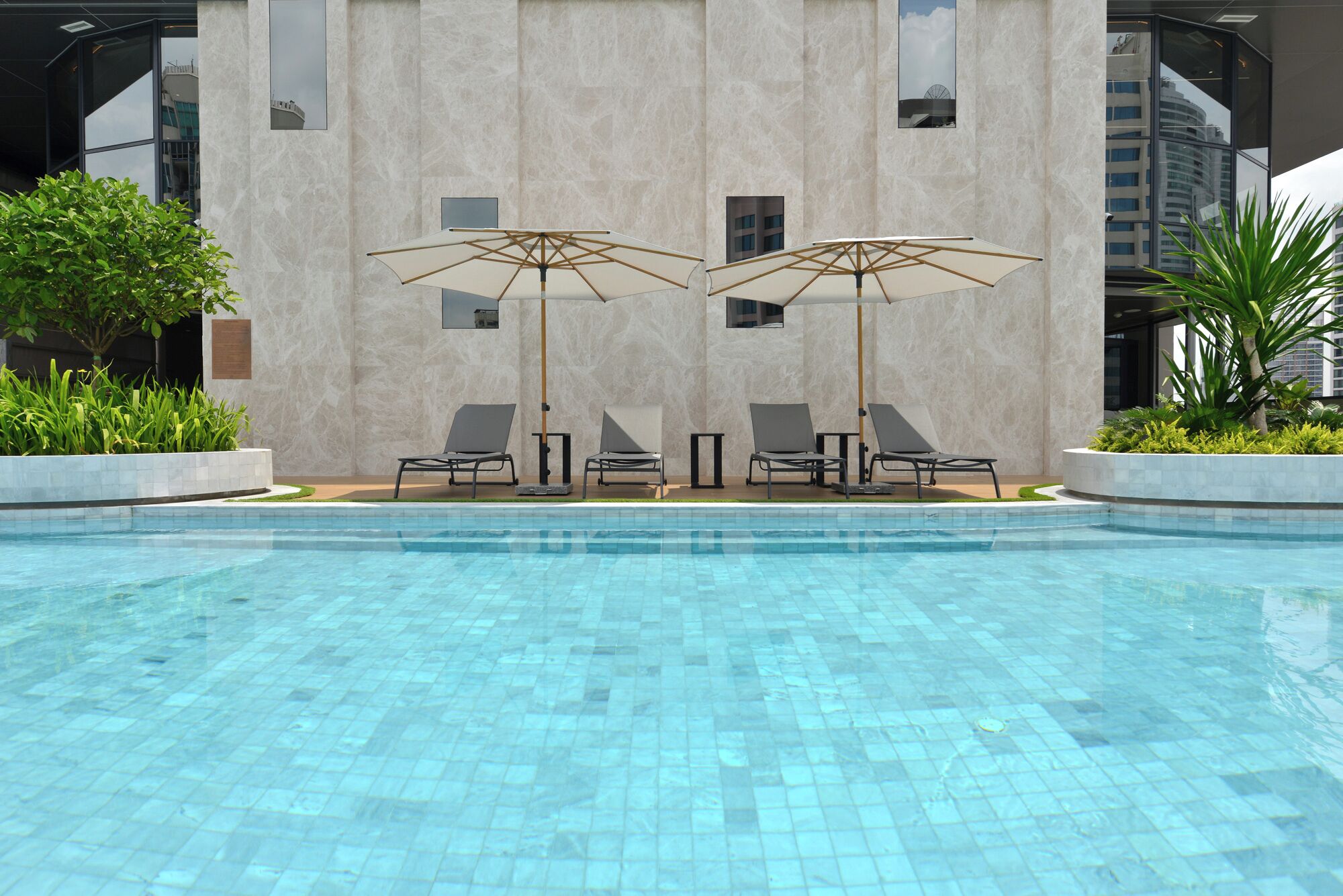 A swimming pool with tiled flooring, surrounded by lounge chairs and umbrellas.