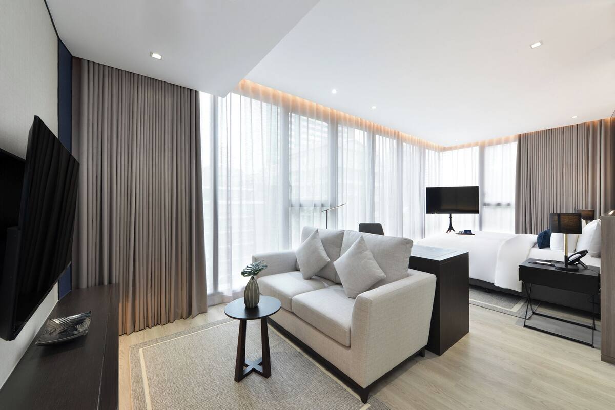 Une chambre d’hôtel moderne équipée d’un canapé, d’un bureau, d’une télévision à écran plat et d’une grande fenêtre avec des rideaux.