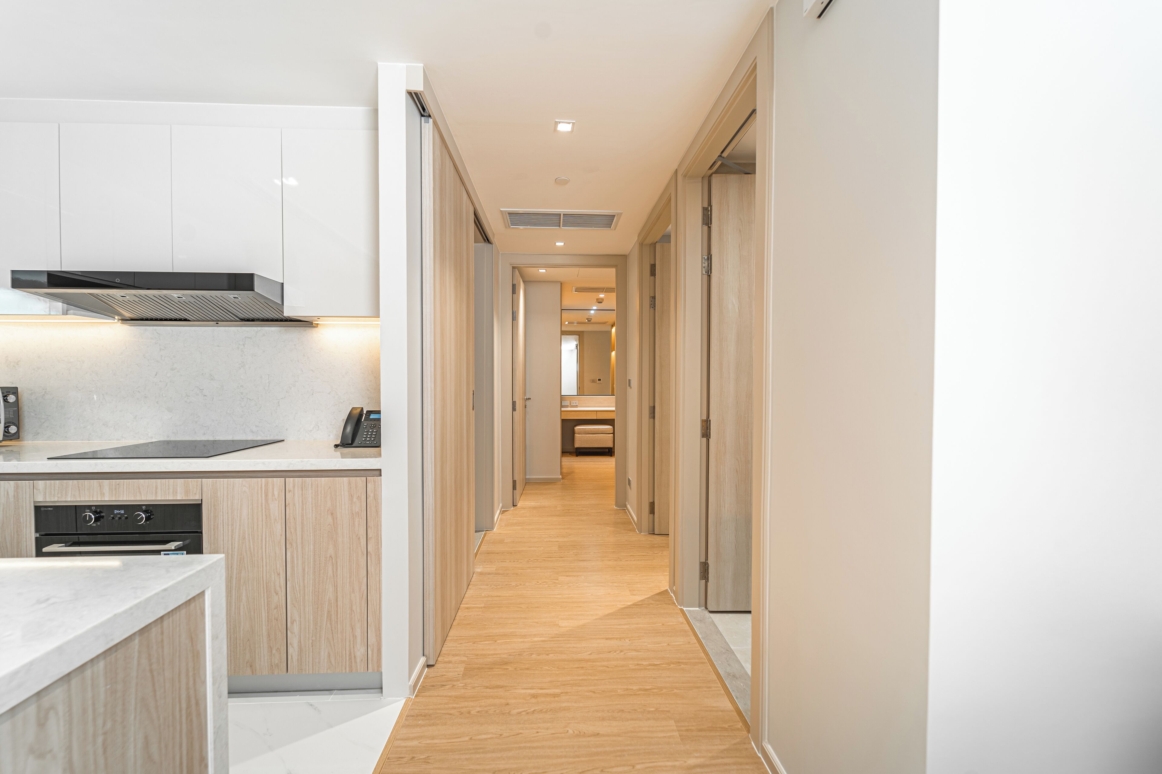A modern kitchen with a wooden floor, white cabinets, and a built-in oven.